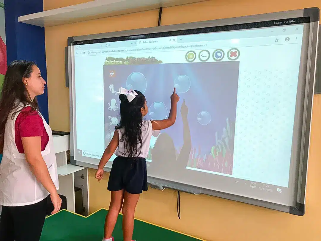 Educadora e criança mexendo em lousa digital