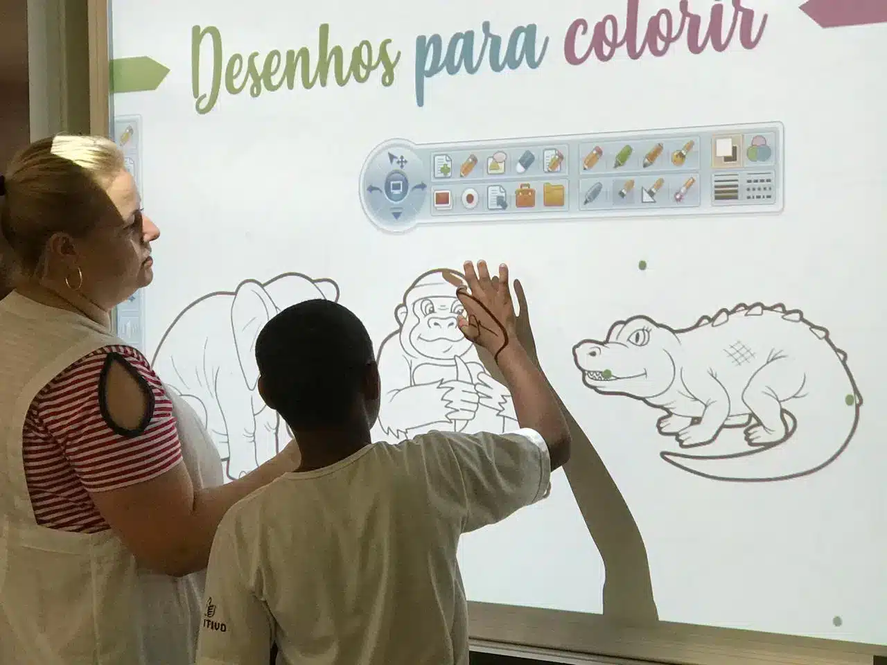 Educadora e jovem aluno juntos usando tela interativa